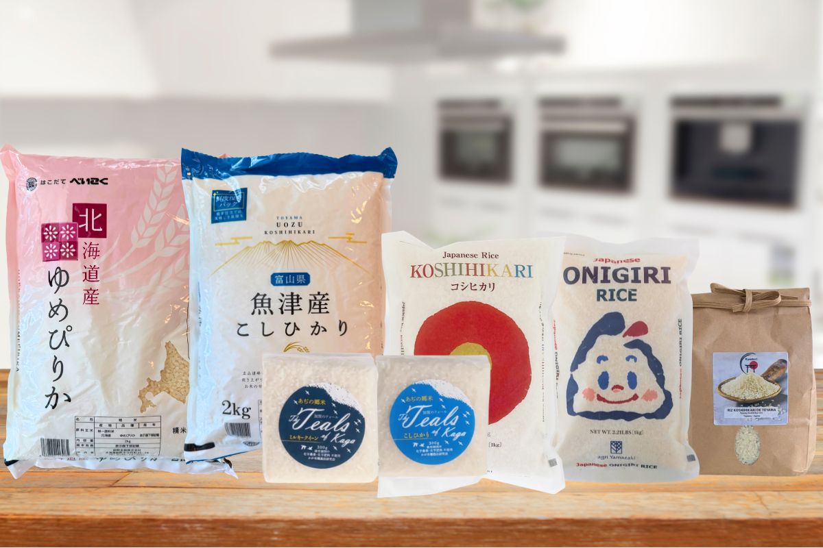 Plusieurs sachets de riz japonais, dont du Yumepirika et du Koshihikari, réunis sur une table en bois devant une cuisine.